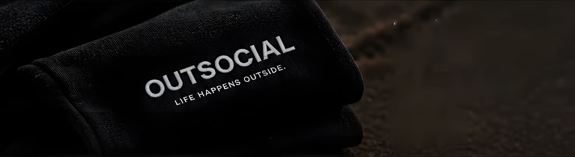 Close up of white OUTSOCIAL, LIFE HAPPENS OUTSIDE. embroidery on a folded black hoodie.
