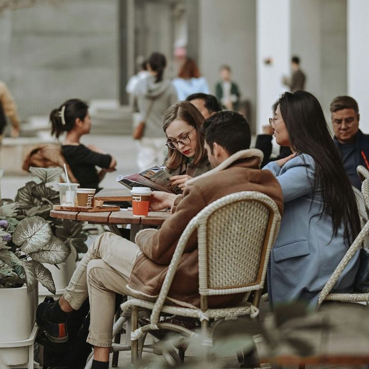 Friends talking over coffee and food at an outdoor cafe table.