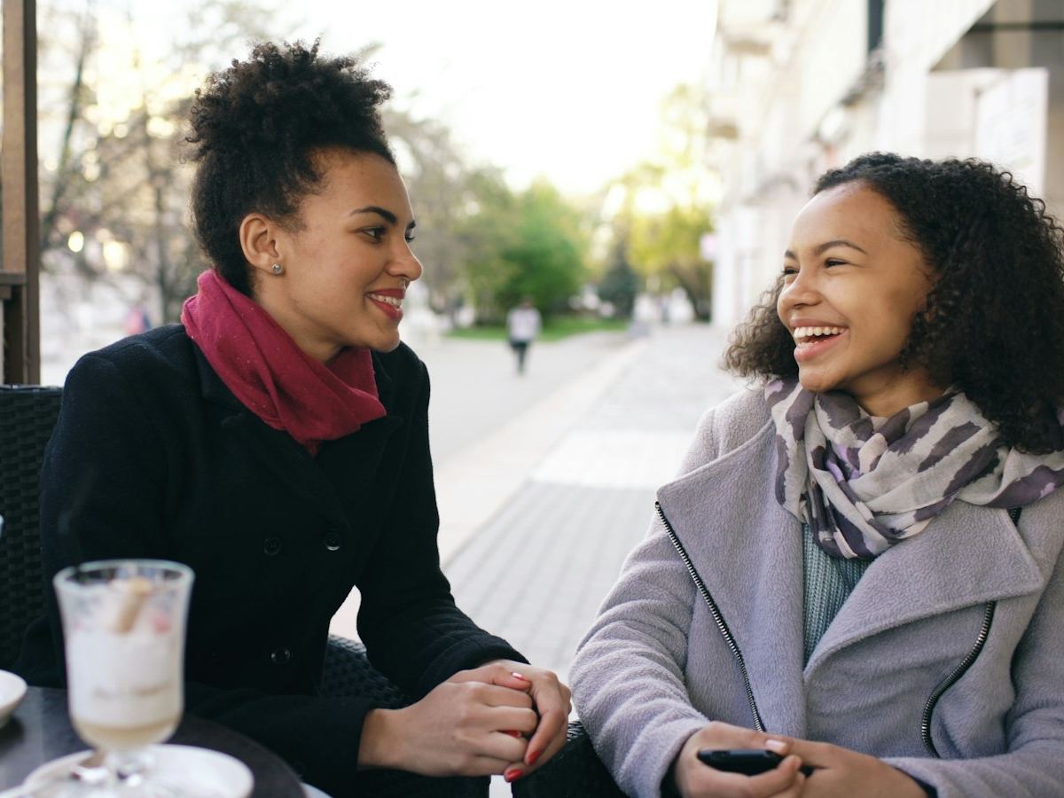Two friends laughing together over coffee at an outdoor cafe.