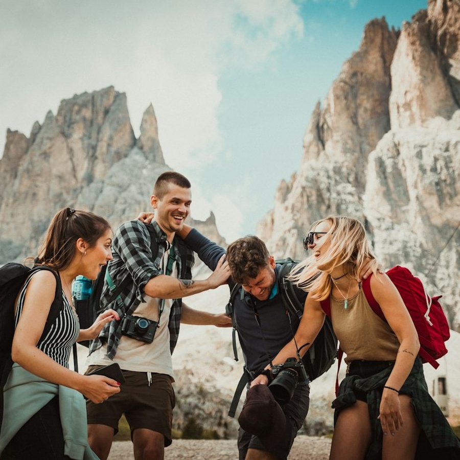 Four friends with backpacks laughing together on a mountain trail.