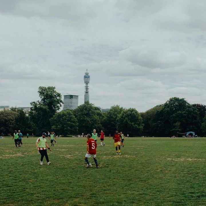 A casual football game on the grass in a London park, with the BT Tower behind the trees.