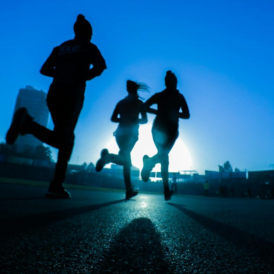 Three runners on a city road at sunrise, running side by side.