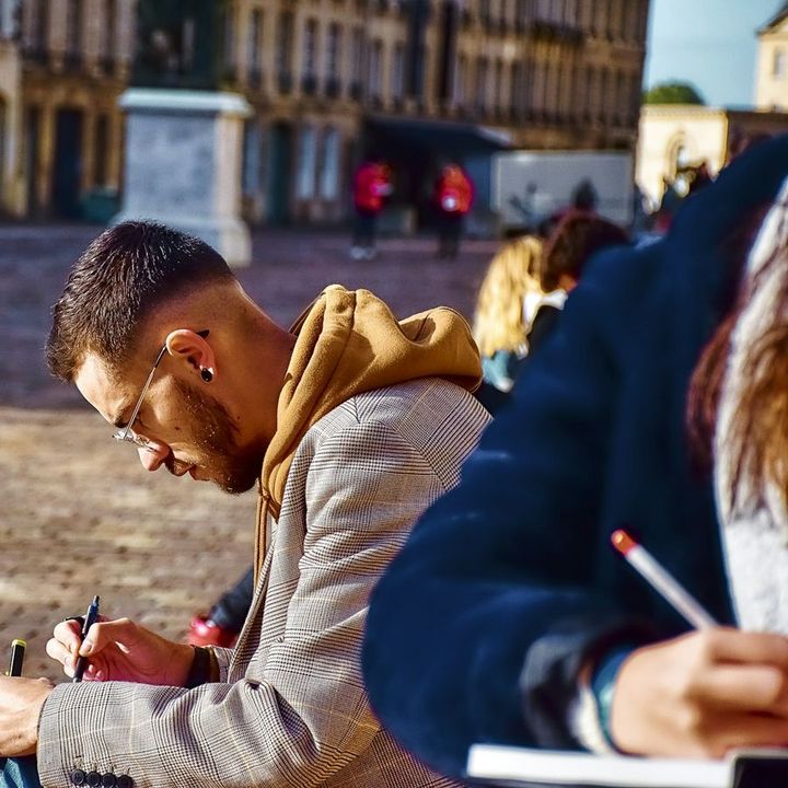 Two people sketching in notebooks in a sunny public square.