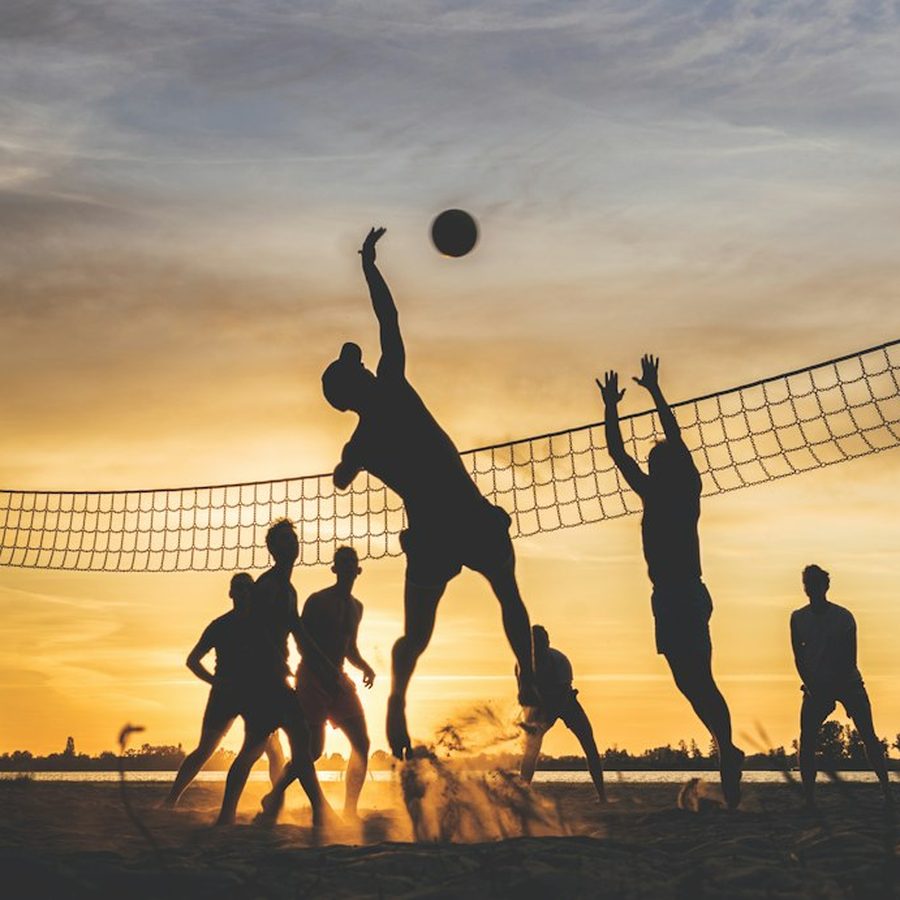 Friends playing beach volleyball at sunset, one leaping for the ball.